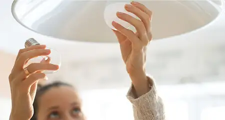 Woman changing LED light bulb on pendant lamp