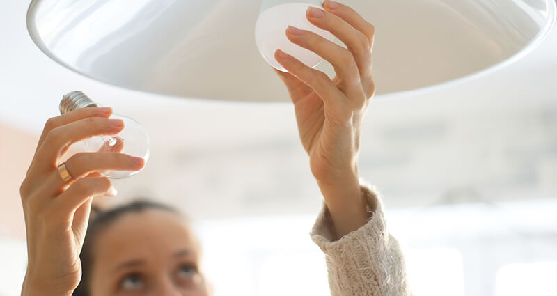 Woman changing LED light bulb on pendant lamp